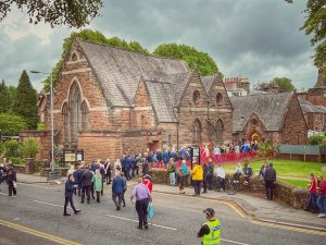 Photo of the outside of The Usual Place building with many people walking towards it and queuing to get in for a special event