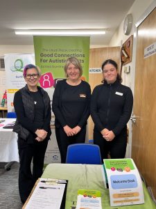 Three women smiling and standing behind leaflets and pop up banner