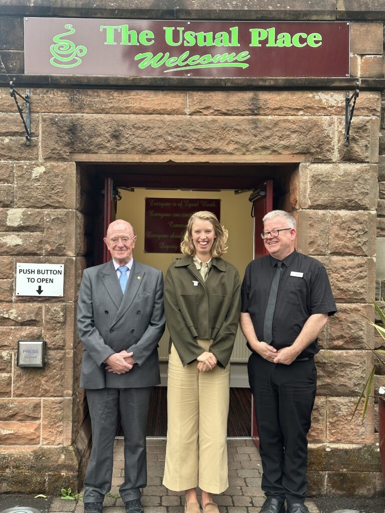 Three people stand in the doorway of The Usual Place. In the centre is Hannah Goodlad, Scottish Minister for Public Finances. Beside her are Russel Griggs, Chair of SOSE and Craig McEwen, CEO of The Usual Place.